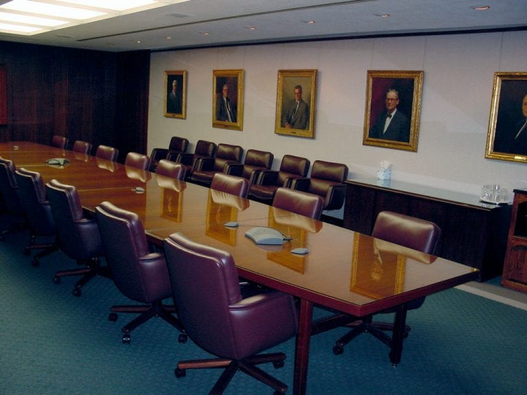 Boardroom at a bank featuring a conference phone and a video screen tastefully enclosed in a wooden cover to blend with the traditional decor.