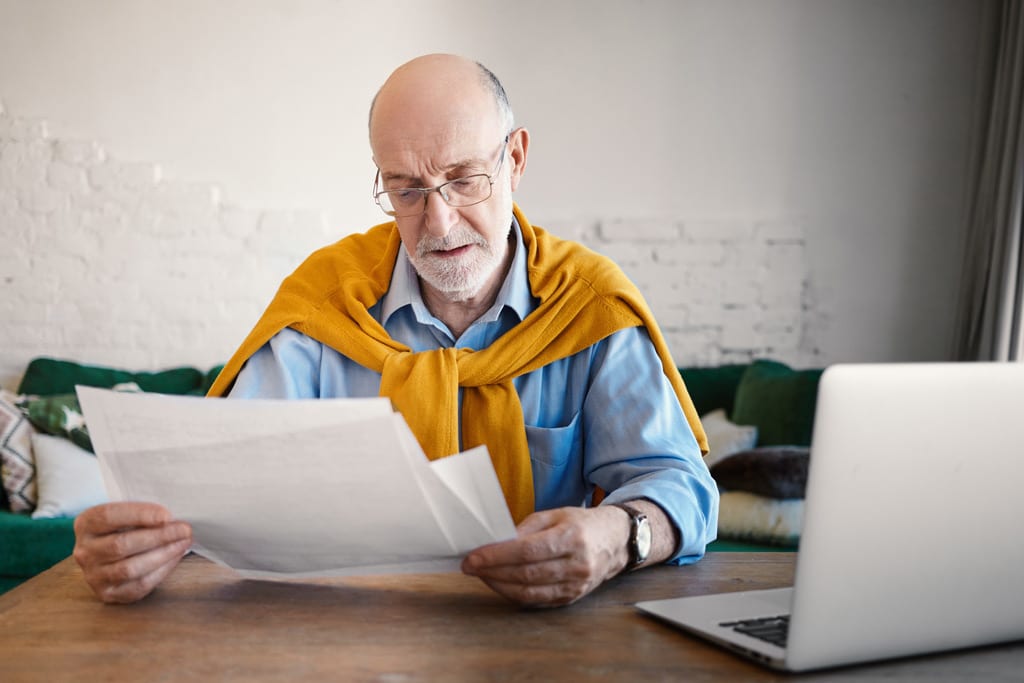 Man with Glasses Reviewing Papers with a Computer